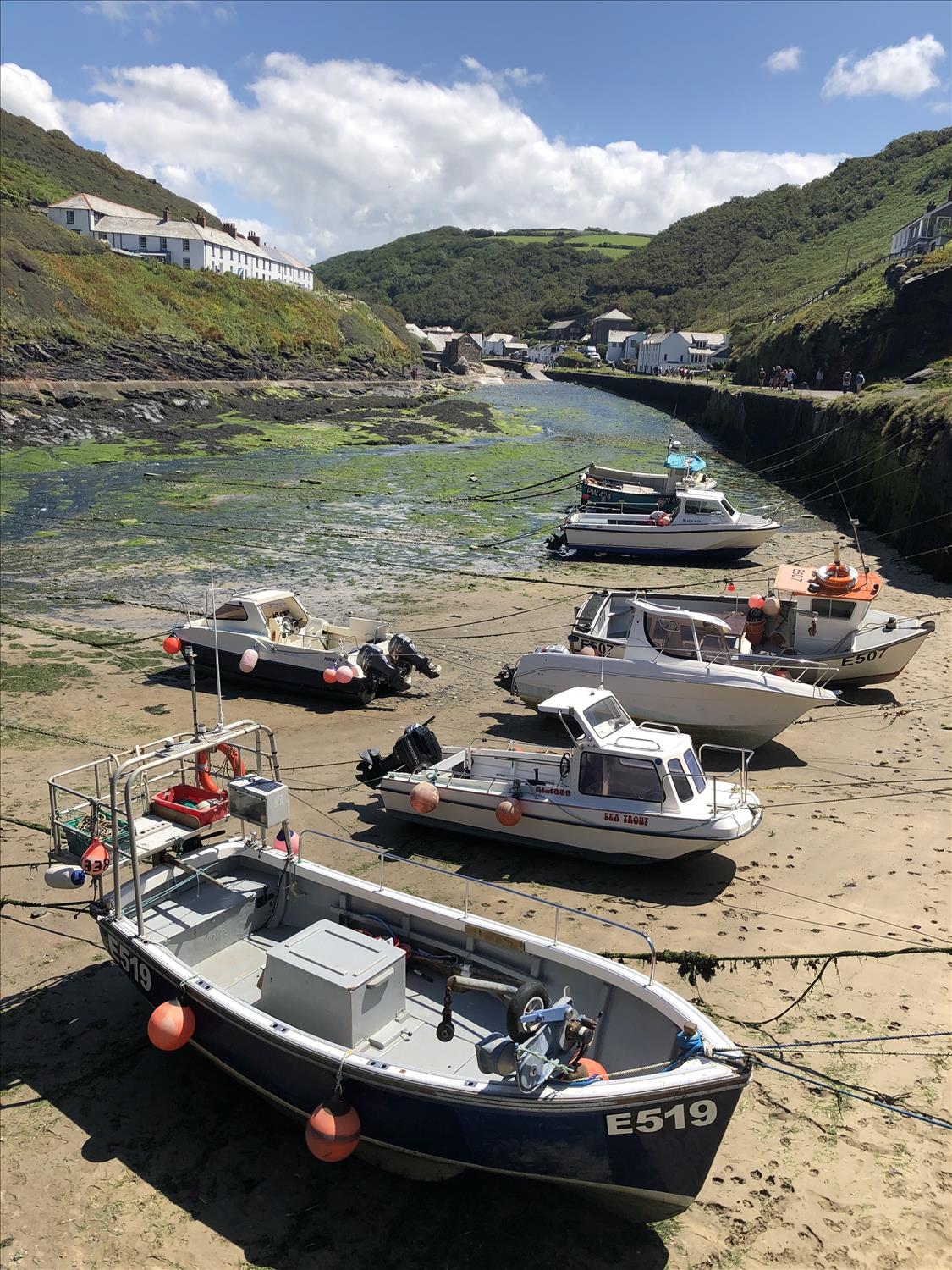 Boats beached with the tide out at Boscastle harbour, Cornwall, with white stone cottages and the hills of the Valency Valley in the background