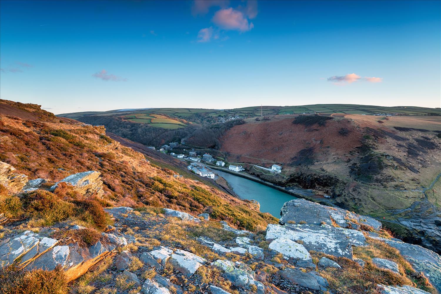 The setting sun gives a burnt orange hue to the heather covering the rocks that frame Boscastle's narrow and twisting harbour, North Cornwall