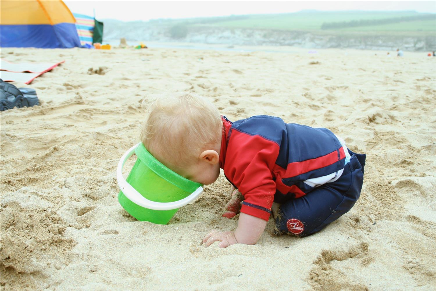 Young boy on the beach closely inspecting the contents of his bucket