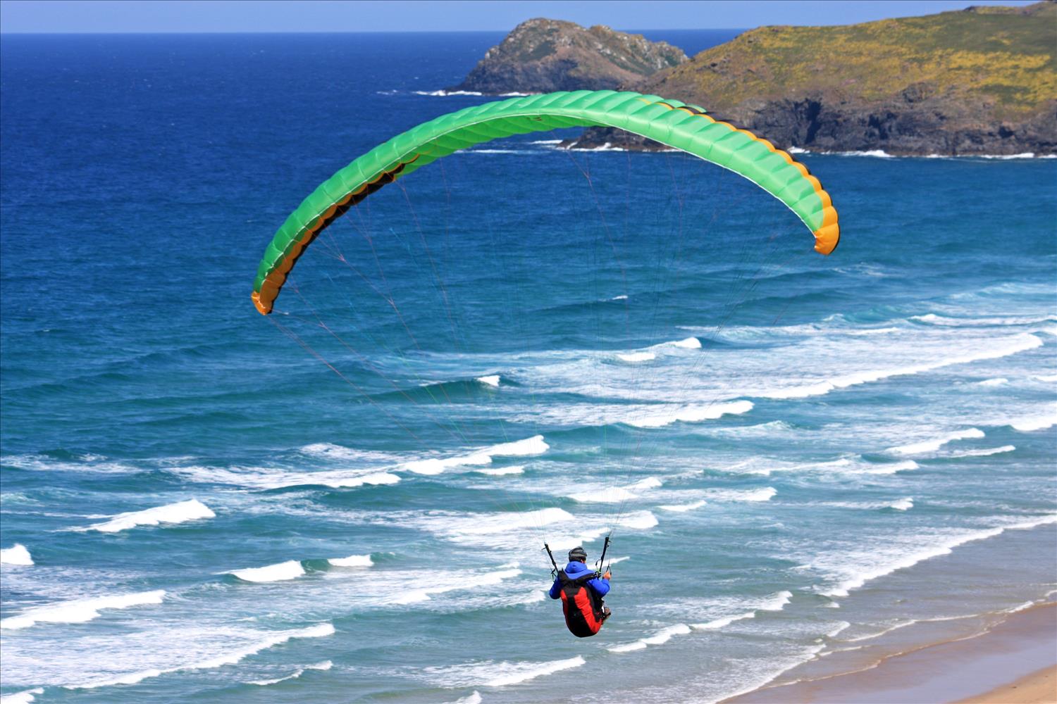 Paraglider flies low over the Atlantic waves at Perranporth, North Cornwall