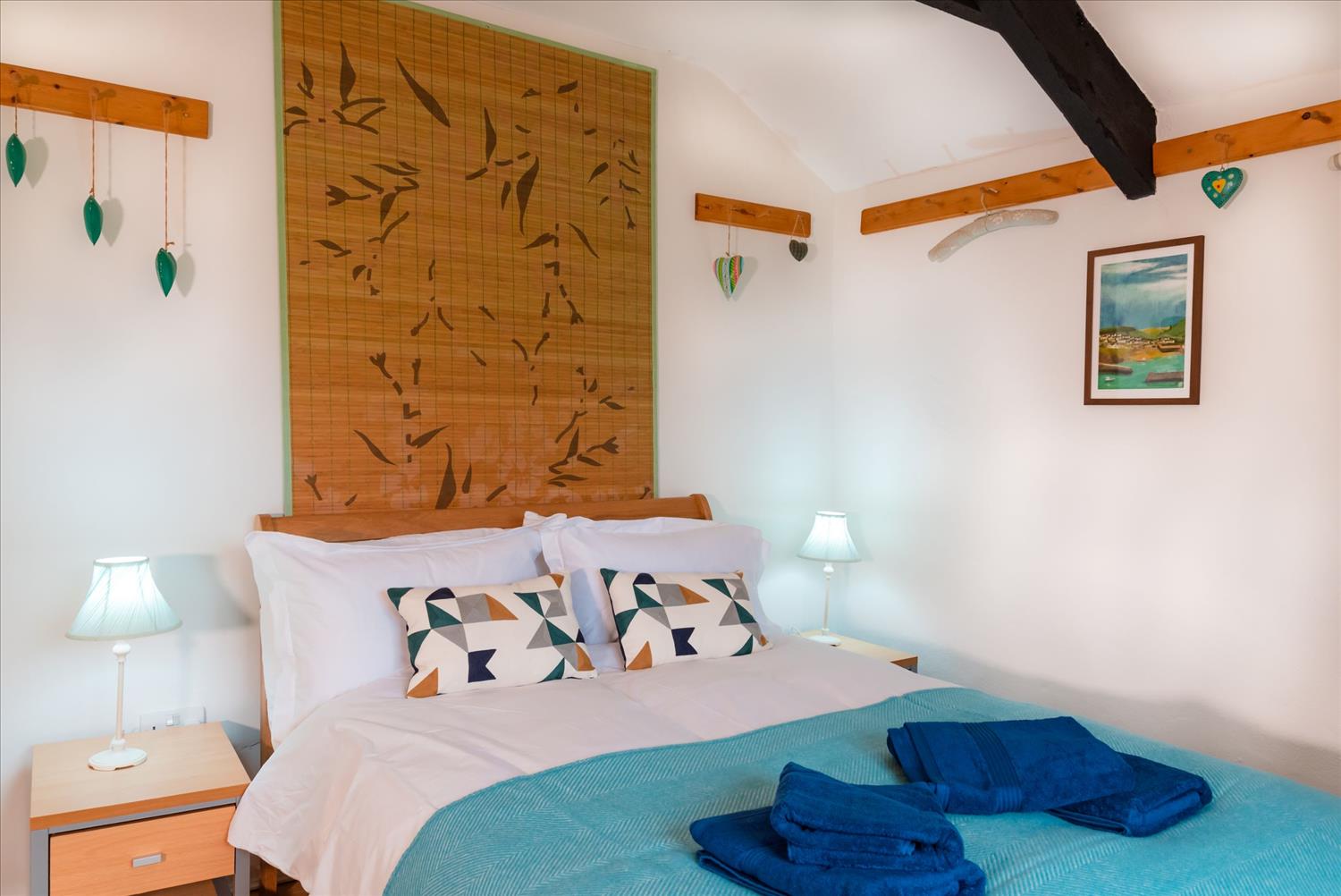 The double-bedroom at Polrunny Farm's Blackberry Cottage, with a towels placed on a blue bedspread; and a picture of Port Isaac on the wall.