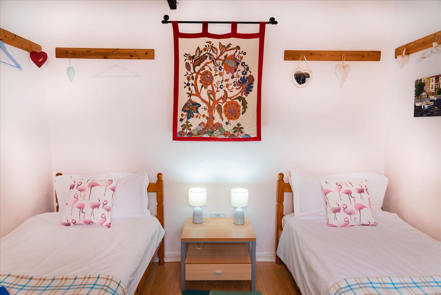 The twin bedroom at Polrunny Farm's Blackberry Cottage, with pink flamingo cushions at the head of the bed and a tapestry on the wall 