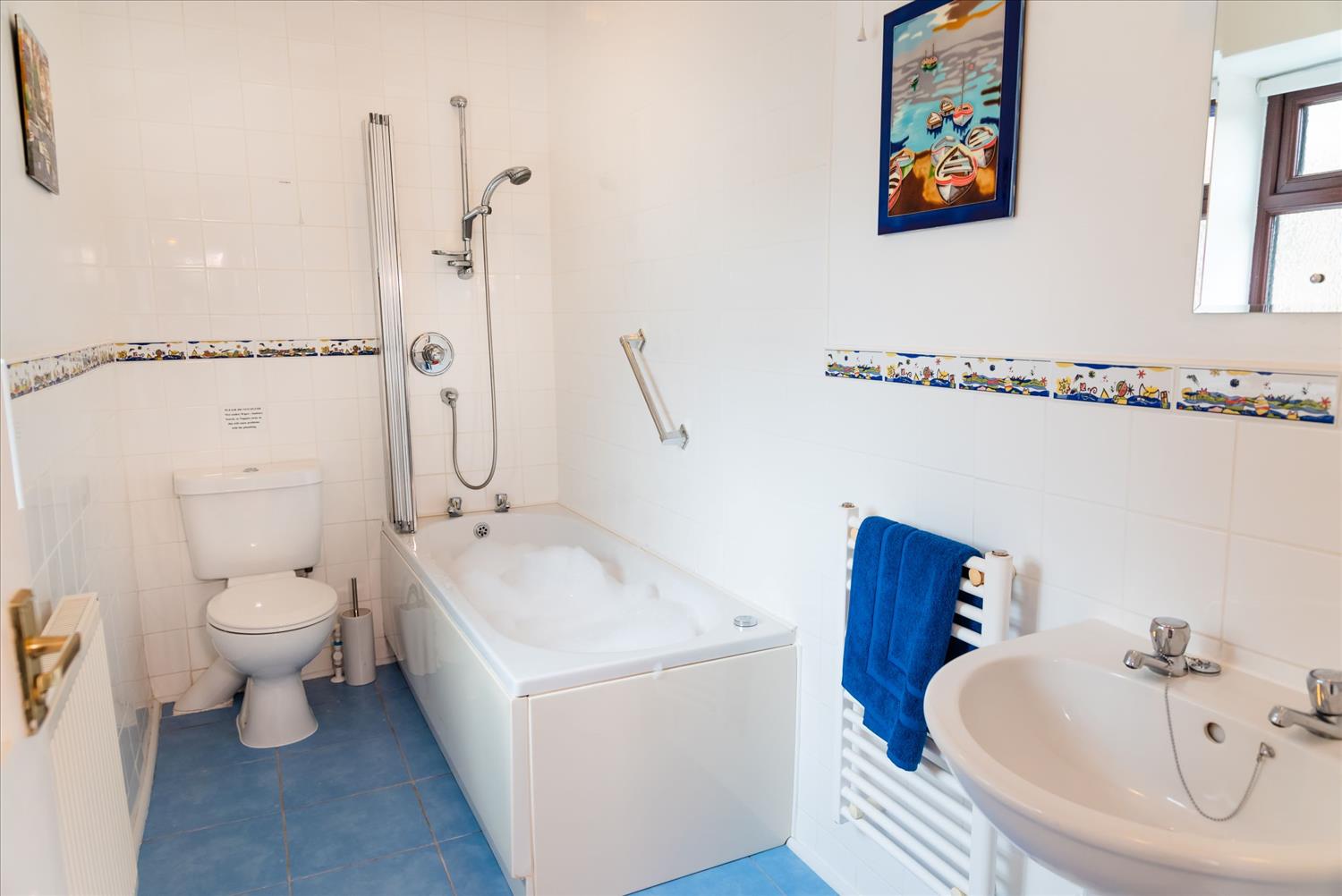 The bathroom at Polrunny Farm's Elderberry Cottage, with foam in the Whirlpool bath and bright coloured pictures on the wall
