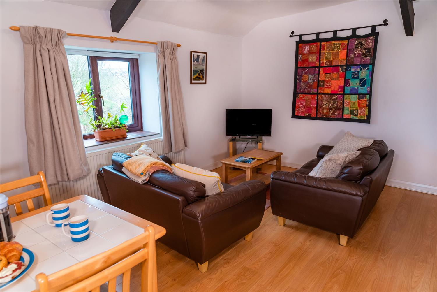 Elderberry Cottage's lounge. As in other properties at Polrunny, a brightly coloured tapestry hangs on the wall above the comfortable brown sofas. 