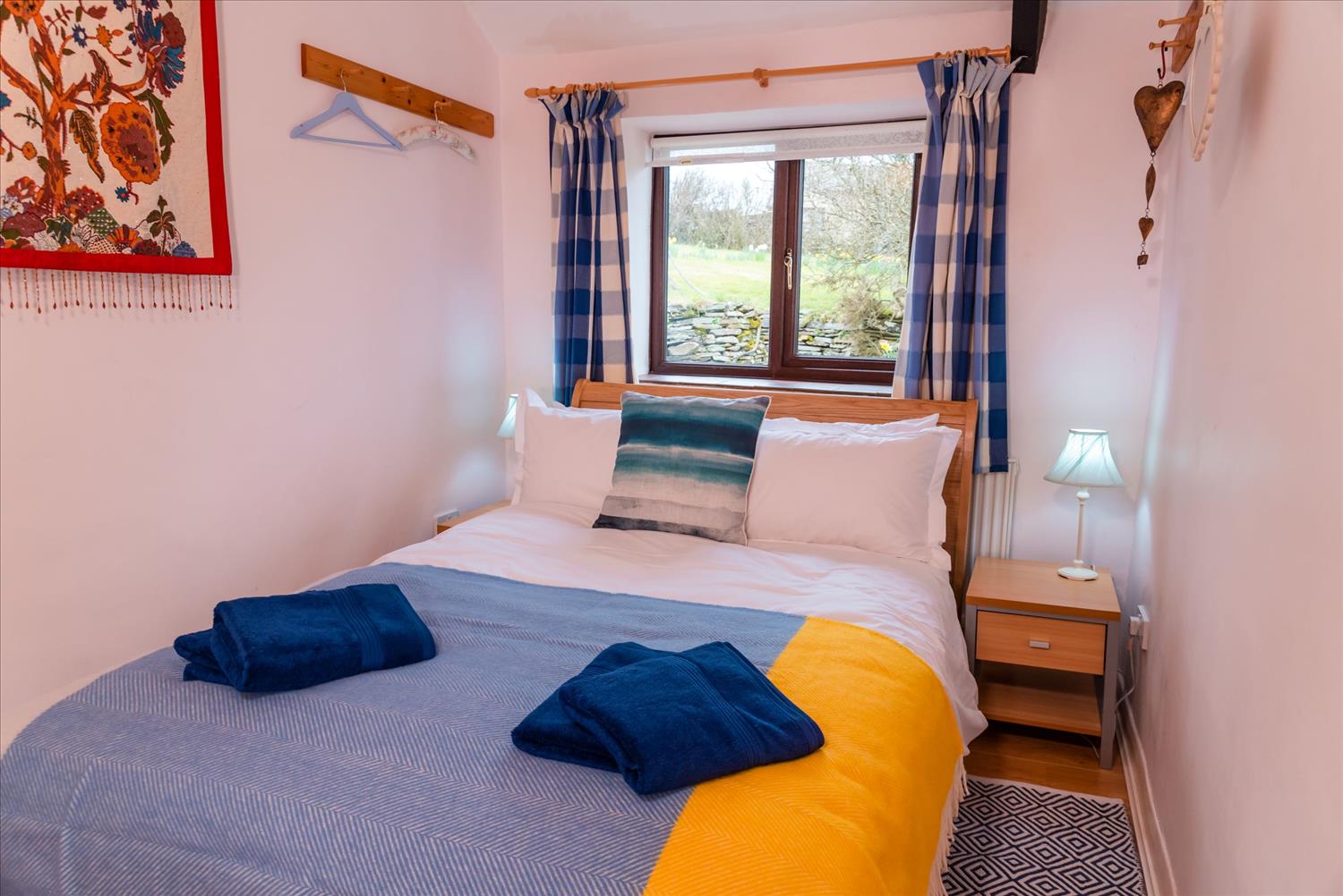 The double bedroom at Polrunny Farm's Elderberry Cottage. The yellows and blues of the throw, the towels and the cushions mirror the colours of the beach and the sea.