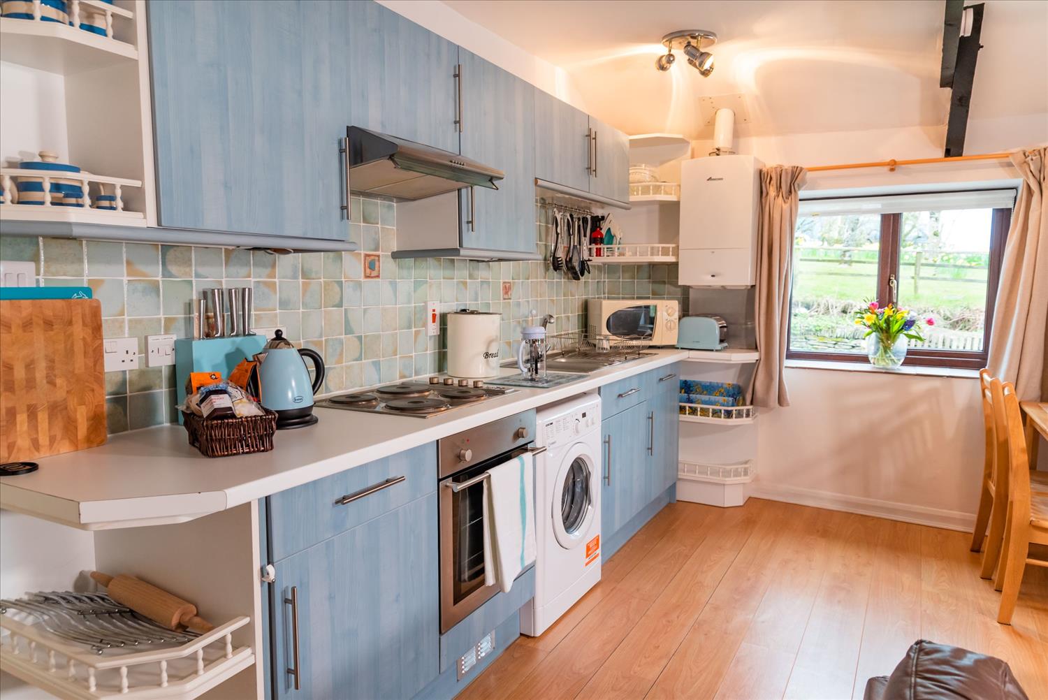 Elderberry Cottage's sea-blue kitchen, with a welcome pack containing Cornish goodies on the worktop and a variety of kitchen spoons and other stuff that I wouldn't know what to do with hanging from hooks on the wall., 
