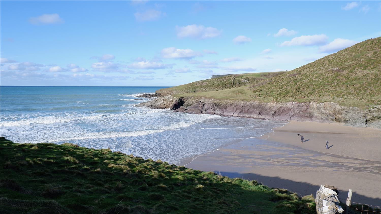 Waves rolling in from the Atlantic lap at the sands of New Polzeath beach, North Cornwall, with the sand deserted but for two people and a dog.