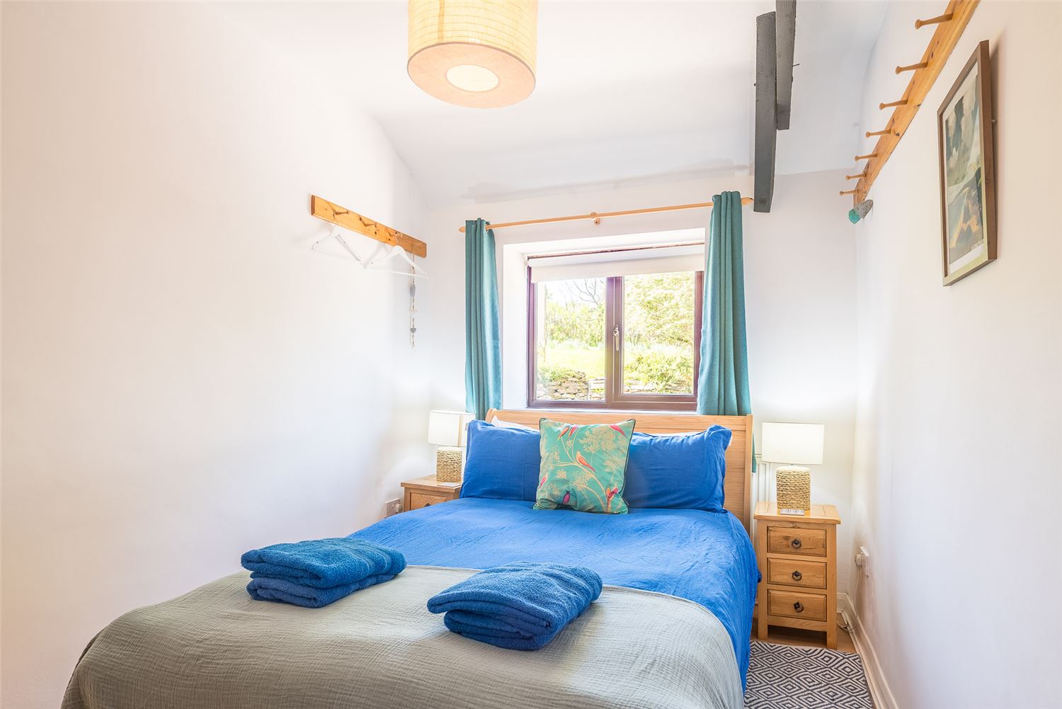 The double bedroom at Polrunny Farm's Elderberry Cottage, with blue towels on the end of the beds, and a tapestry hung on the wall